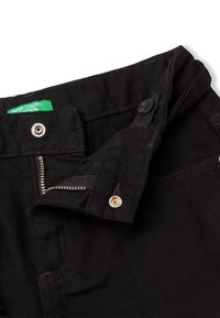 Černé džíny vyrobené z denimu s poklopcem na zip a knoflíkovým zapínáním, se zelenou etiketou s nápisem "UNITED COLORS" a viditelnými švy.