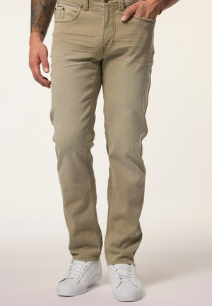 Jeans ajustados color marrón claro, hechos de denim, con cinco bolsillos y cierre de cremallera, combinados con zapatillas blancas. Textura suave y diseño clásico.