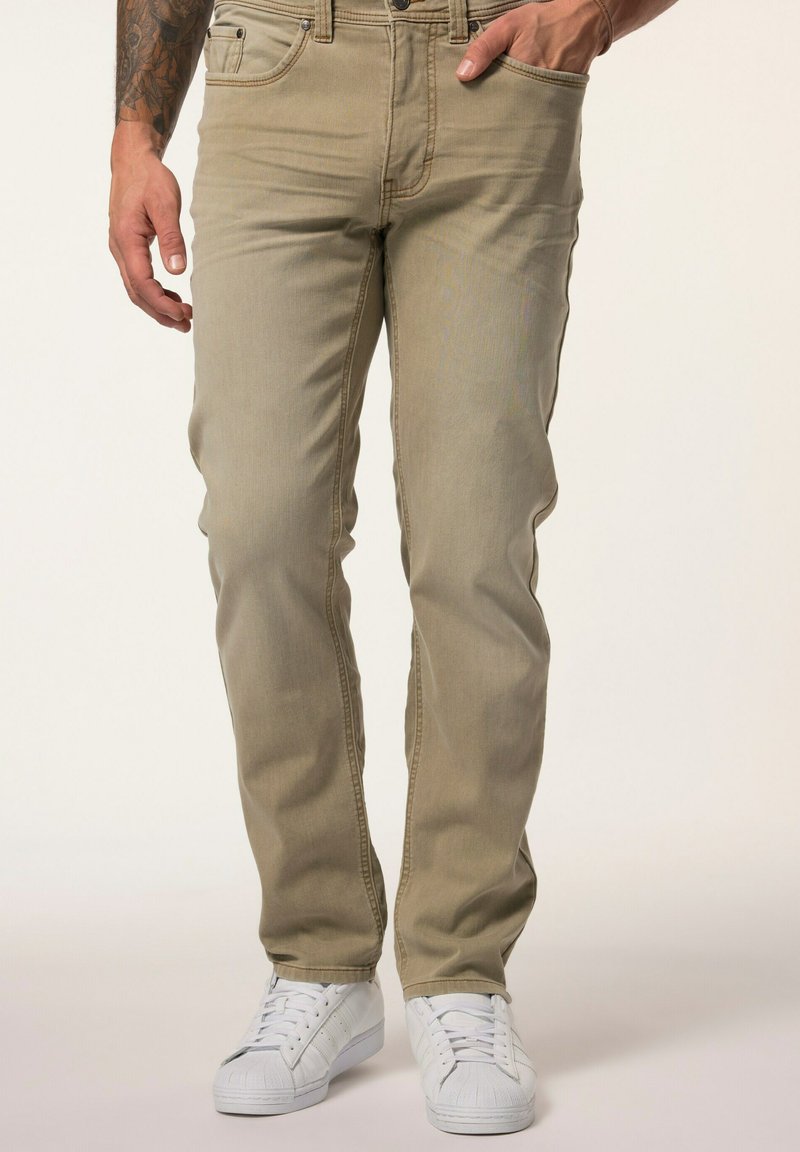 Jeans ajustados color marrón claro, hechos de denim, con cinco bolsillos y cierre de cremallera, combinados con zapatillas blancas. Textura suave y diseño clásico.