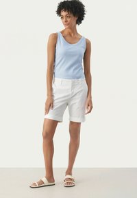 Top senza maniche azzurro chiaro, pantaloni corti bianchi fino al ginocchio con orli risvoltati, e sandali beige. Tessuto morbido e vestibilità rilassata in tutto.