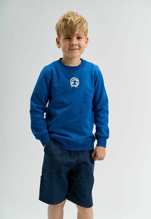 Blå bomulds sweatshirt med lange ærmer og ribbede manchetter, med et centralt hvidt logo; parret med mørke denim shorts.