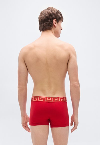 Κόκκινα αντρικά εσώρουχα boxer από ελαστικό ύφασμα με ζώνη μέσης σε χρυσό χρώμα διακοσμημένη με το ελληνικό κλειδί, σχεδιασμένα για εφαρμογή που αγκαλιάζει το σώμα, σε προβολή από πίσω.