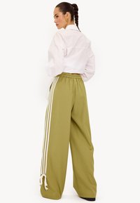 Groene wijde broek met witte strepen aan de zijkanten, elastische tailleband en een relaxte pasvorm. Gecombineerd met een wit shirt.