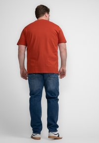 Camiseta de manga corta color óxido combinada con jeans de mezclilla azules. Los jeans tienen dos bolsillos traseros y un corte relajado. Incluye calzado informal.