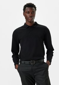 Zwarte lange mouwen polo shirt van een gestructureerde stof, met een drieknops sluiting en een op maat gemaakte pasvorm, gecombineerd met zwarte slim-fit broek en een riem.