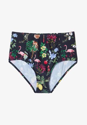 Gros plan d'une personne portant un bas taille haute foncé et un haut avec un imprimé coloré d'oiseaux tropicaux, coquillages, fleurs et singes.
