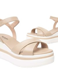 Sandali platform beige con cinturini incrociati, texture liscia e una spessa suola bianca. Notabili per il loro design minimalista e il comfort.