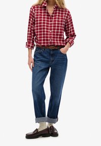 Camicia con bottoni a quadri rossi e bianchi abbinata a jeans di denim blu. Indossata con mocassini scuri e calzini color crema. Vestibilità casual.