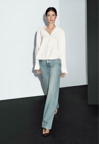 Vit långärmad skjorta med knappar, i kombination med ljusblå vida jeans och bruna sandaler, med en avslappnad passform och mjuk textur.