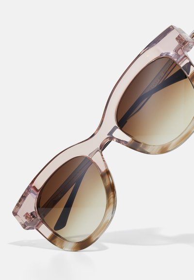 Lunettes de soleil teintées de rose avec un design massif, dotées de verres dégradés marron et d'accents marron clair sur les bords de la monture et les branches.