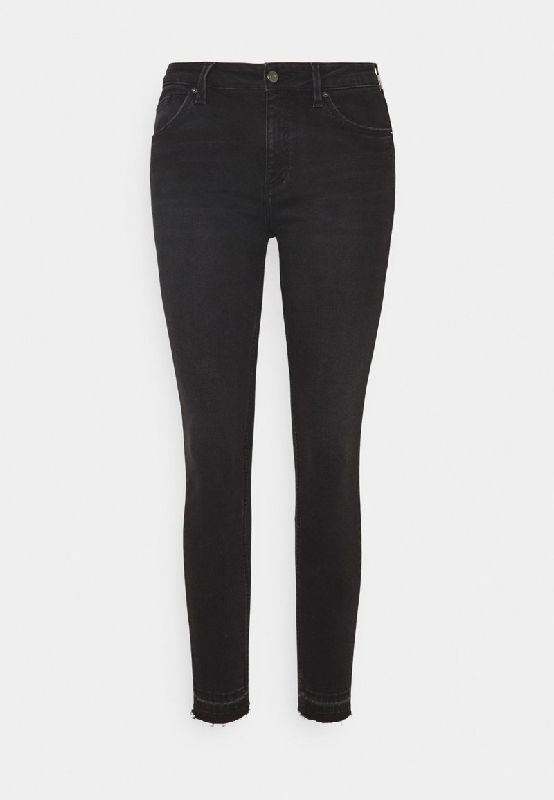 Jean skinny noir taille haute avec fermeture boutons et zip, poches avant et ourlets effilochés sur un fond clair.