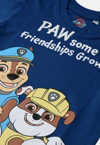 Niebieska bawełniana koszulka z grafiką rysunkowych psów, jeden w niebieskiej czapce, a drugi w żółtej czapce, z napisem "Wspaniałe Przyjaźnie Rosną".