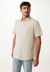 Camisa de manga corta en un tejido transpirable color beige claro, con frente abotonado y cuello clásico, combinada con unos vaqueros azul claro.