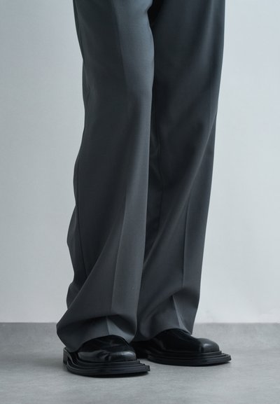 Šedé široké kalhoty s hladkou strukturou v kombinaci s černými leštěnými mokasíny se zrnitou podešví.