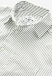Camisa de cuello a rayas verde clara y blanca con un ajuste relajado, que cuenta con un bolsillo en el pecho y botones blancos. Tela suave, diseño a medida.