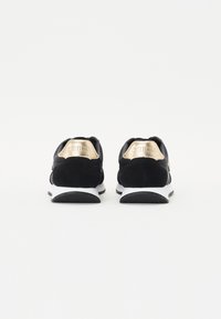 Svarte semskede sneakers med gullakenter på hælen, har en hvit mellomsåle og svart gummisåle. Enkelt og sporty design.