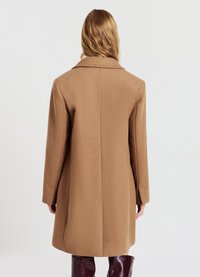 Cappotto di lana marrone con un design strutturato, maniche lunghe e colletto a lancia. Tessuto testurizzato e taglio dritto, che arriva a metà coscia.