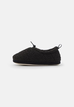 Black fleece slipper with rounded toe, adjustable toggle closure, and flat beige sole, viewed from the side on a plain background.