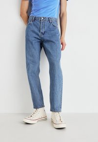Light blue denim jeans with a straight leg fit, five pockets, and a classic button closure, paired with off-white sneakers.