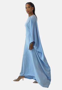 Helles blaues langes Kleid mit weiten Ärmeln, fließendem Stoff und glatter Textur. Kombiniert mit beigen Absätzen, die ein metallisches Akzent haben.
