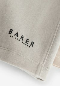 Světlá šedá tkanina s jemnou texturou, na které je černý text "BAKER" a "by TED BAKER". Viditelné švy podél okrajů.