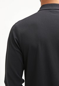 Musta pitkähihainen poolopaita, jossa on teksturoitu kangas, klassinen kaulus ja suora takasuunnittelu.