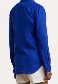 Blå linne skjorta med lång ärm, knäppning vid ärmsluten och en slät yta. Har en klassisk krage och en avslappnad passform.