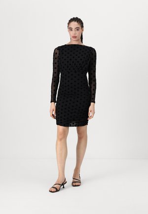 Schwarzes Kleid mit Polka-Dots, transparenten langen Ärmeln, Raffung und taillierter Silhouette, kombiniert mit schwarzen Riemchen-Heels.