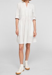 Robe blanche à rayures avec un décolleté en V, des manches courtes, une taille froncée et deux poches poitrine, associée à des baskets montantes blanches.