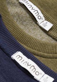 Dwie dzianinowe koszulki w oliwkowej zieleni i granatowym, z prążkowanymi kołnierzykami. Metki wskazują markę „minymo” oraz rozmiar 5/110. Widoczna miękka tekstura.