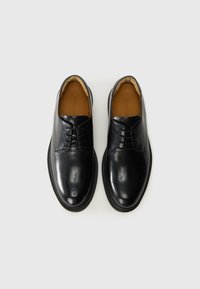 Pantofi din piele neagră cu o textură netedă, vârf rotunjit, design cu șireturi și o căptușeală subtilă în nuanță de bej. Talpă plată din cauciuc.