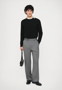 Mustra must cardigan, hall riba pinstriped püksid, mustad kingad. Hoides musta õlakotti. Minimalistlik disain, sile tekstuur.