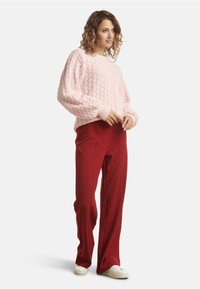 Pink textured knit sweater with a block pattern, paired with red wide-leg pants and white sneakers. Soft materials, casual fit.