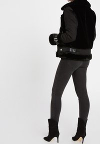 Černá umělá kožešinová bunda s hladkou texturou, s stojáčkovým límcem a detaily na sponách. Spárována s tmavými úzkými džíny a černými kotníkovými botami.