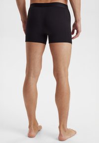 Černé bavlněné boxerky s těsným, elastickým pasem. Tkanina vypadá hladce a těsně, prezentuje minimalistický design.