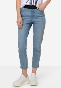 Pantalones de mezclilla cortos en un azul claro con una cinturilla negra, que presentan un diseño ajustado, un ligero desvanecimiento y detalles en las costuras laterales. Combinados con zapatillas blancas.
