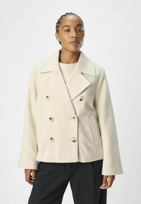 Veste double boutonnage beige clair avec un large col, de grands boutons ronds et des poches latérales ; tissu texturé et coupe décontractée.