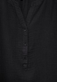 Camicia nera con bottoni e scollatura a V, realizzata in tessuto testurizzato. Presenta una patta con sei bottoni e una vestibilità rilassata.