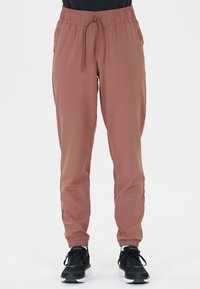 Leichte, staubige Rose Jogginghosen mit elastischem Bund, Kordelzug, Seitentaschen und gerippten Knöcheln. Kombiniert mit schwarzen Turnschuhen.