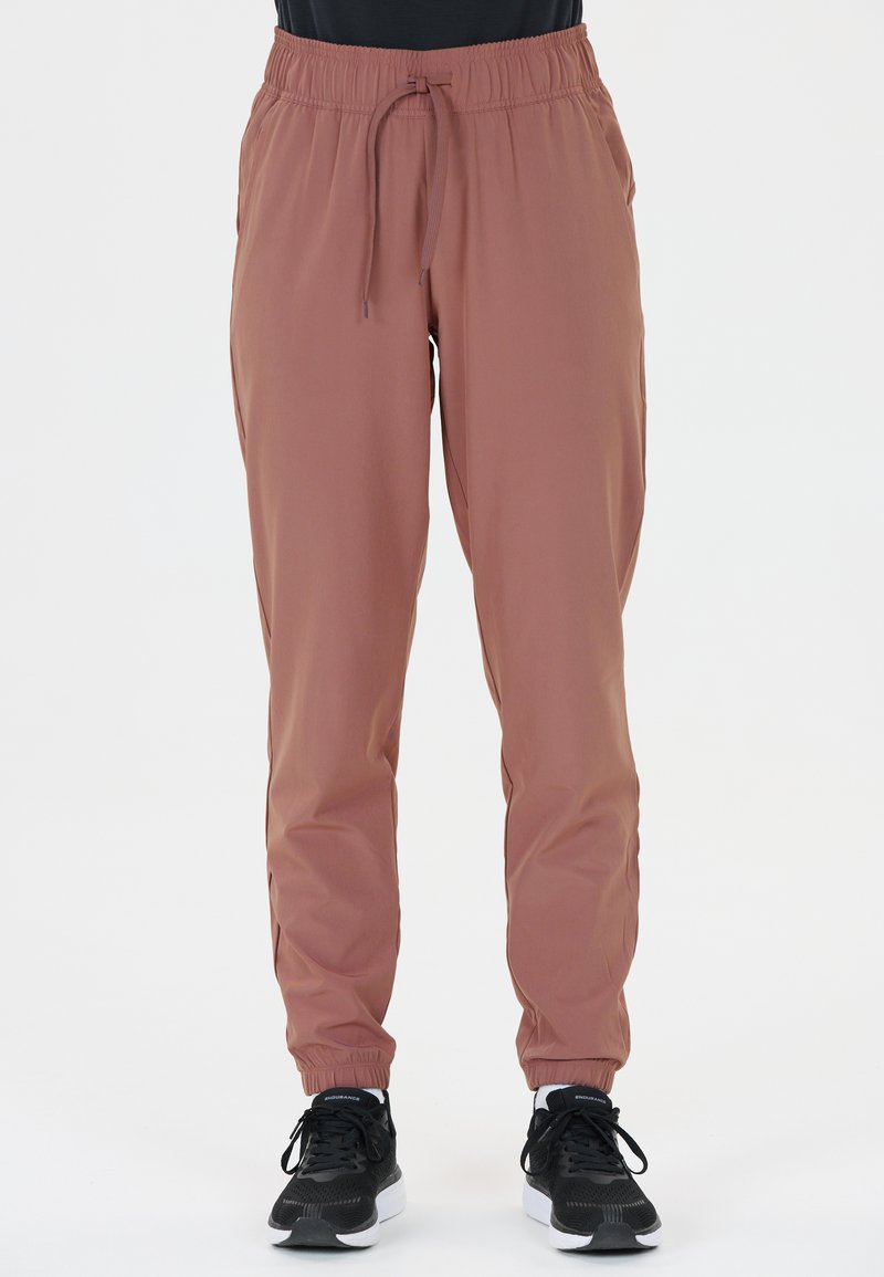 Leichte, staubige Rose Jogginghosen mit elastischem Bund, Kordelzug, Seitentaschen und gerippten Knöcheln. Kombiniert mit schwarzen Turnschuhen.