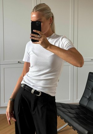 Witte korte mouw T-shirt gecombineerd met zwarte broek, voorzien van een zilveren gesp riem. Soepele stof met een aansluitende snit, minimalistische stijl.