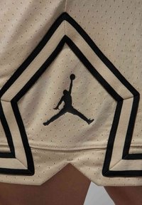 Pantalones cortos deportivos beige con un diseño de chevron en blanco y negro, con textura perforada y un destacado logo de Jordan en negro en la parte inferior.