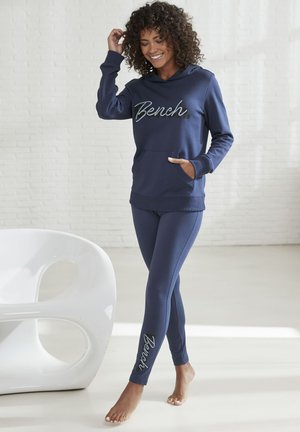 Navyblaues Sweatshirt mit "Bench"-Logo und Fronttasche, kombiniert mit passenden Leggings, die am Knöchel ein Logo haben und aus weichem Material bestehen.