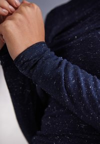 Námořnická modrá dlouhá rukávová košile s měkkou, texturovanou tkaninou a stříbrnými fleky, s pečlivě provedeným stehem na manžetách a těsným střihem kolem zápěstí.