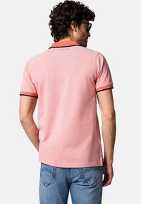 Różowa koszulka polo o teksturowanym wykończeniu, z czarnym wykończeniem na kołnierzu i rękawach. Kontrastowe przeszycia i detal z logo z tyłu.