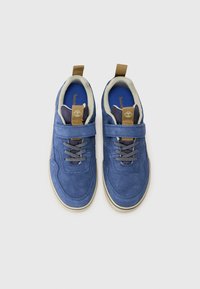Plave suede cipele s bež unutarnjim oblogom, ravnim vezicama i čičak trakom oko srednjeg dijela. Ima malu oznaku s logotipom na jeziku.