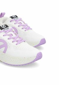 Weiße Sportschuhe mit helllila Akzenten, einer strukturierten Oberfläche und einer gepunkteten Sohle. Sie verfügen über flache Schnürsenkel und ein Logo auf der Zunge.