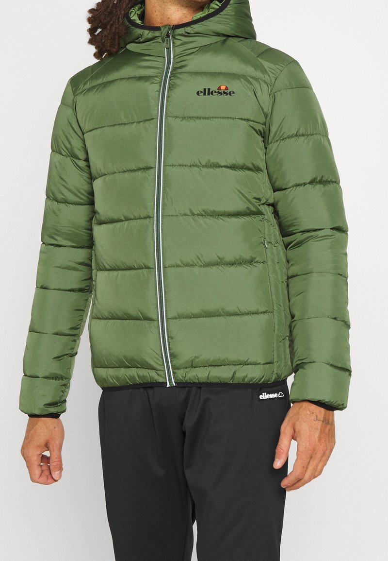 Zelená puffer bunda s kapucí, se zipovým uzavíráním, žebrovanými manžetami a vyšitým logem na hrudi. Hladká textura a prošívaný design.