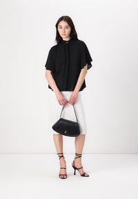 Blusa nera a maniche corte con fronte texturizzato, gonna bianca sopra il ginocchio, tacchi neri con cinturini e borsa nera con un dettaglio dorato.