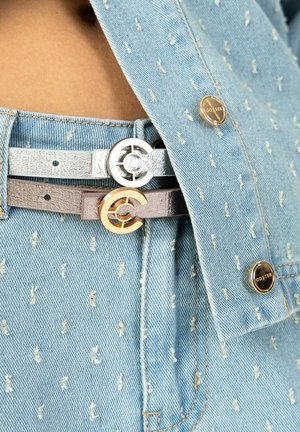 Due cinture in argento e taupe con motivi goffrati, caratterizzate da fibbie con logo, indossate con una maglia in denim azzurro chiaro testurizzata.